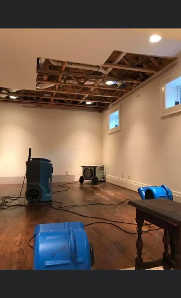 Water damage restoration in progress - dehumidifiers and air movers drying a basement with ceiling removed by Property Restoration Pros